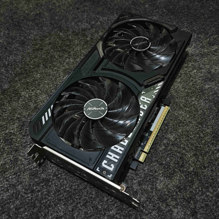 An overhead, angled shot of an ASRock Challenger Radeon graphics card resting on a dark, textured grey surface. The card features a dual-fan cooling system with sleek, black serrated blades. The fan on the left is branded with the ASRock logo, while the fan on the right displays the Challenger logo. The shroud is predominantly matte black with industrial accents, including white "CHALLENGER" text printed along the bottom edge and silver-toned decorative stripes. The gold contacts of the PCIe interface and the silver rear I/O bracket are visible at the bottom and left sides of the card.