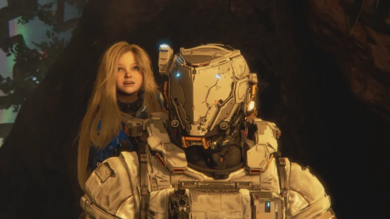 An image from a video game featuring two characters: a young girl with long blonde hair and a large, armored figure in a high-tech white suit. The girl stands behind the armored character, looking upward with a hopeful, curious expression. The armored character wears a bulky white helmet with glowing blue lights for eyes and intricate mechanical details. They appear to be in a dimly lit, cave-like environment with dark rocky textures in the background.